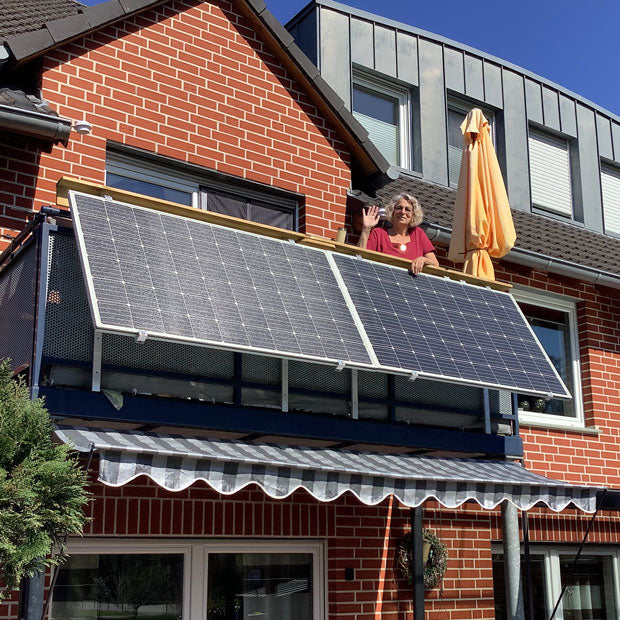 Balkon mit Solarmodulen und winkender Frau